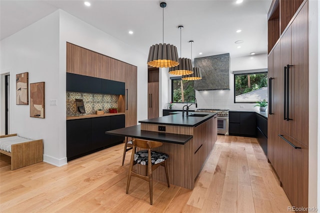 kitchen with a center island with sink, tasteful backsplash, light wood-type flooring, high end range, and pendant lighting