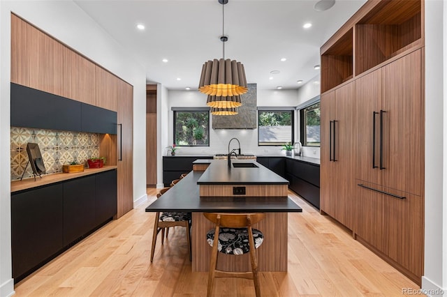 kitchen featuring an island with sink, hanging light fixtures, light wood-type flooring, and tasteful backsplash