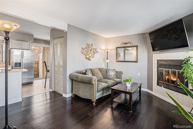 living room with dark wood-style floors, a textured ceiling, a fireplace, and baseboards