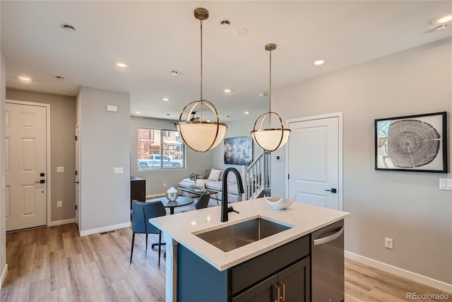 kitchen featuring dishwasher, sink, hanging light fixtures, light hardwood / wood-style flooring, and a center island with sink