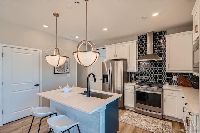 kitchen featuring wall chimney exhaust hood, stainless steel appliances, a kitchen island with sink, sink, and decorative light fixtures