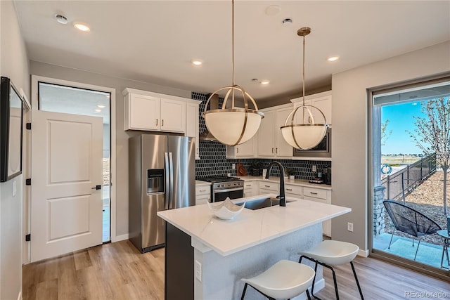 kitchen with sink, appliances with stainless steel finishes, pendant lighting, white cabinets, and light wood-type flooring