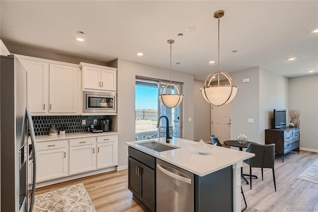 kitchen with white cabinets, a center island with sink, sink, hanging light fixtures, and stainless steel appliances