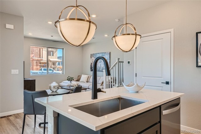 kitchen with a center island with sink, sink, stainless steel dishwasher, light wood-type flooring, and decorative light fixtures