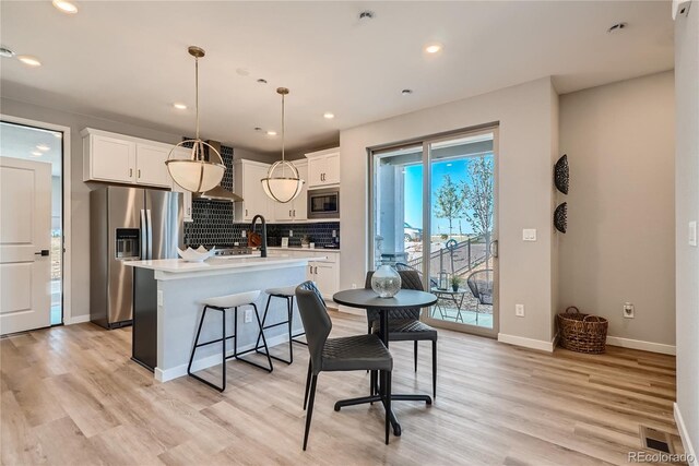 kitchen with pendant lighting, backsplash, a kitchen island with sink, white cabinetry, and stainless steel appliances