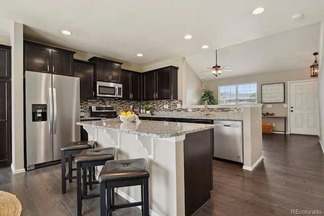 kitchen featuring a ceiling fan, light stone counters, a peninsula, backsplash, and appliances with stainless steel finishes