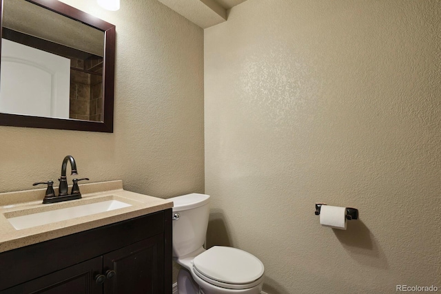 half bathroom with toilet, vanity, and a textured wall