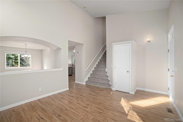 unfurnished living room featuring a towering ceiling, wood-type flooring, a chandelier, and sink