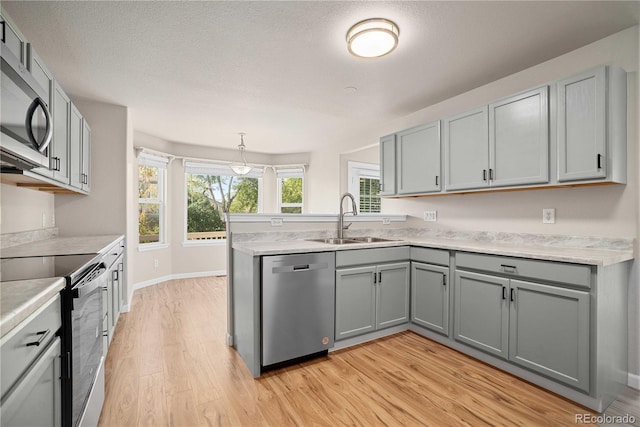 kitchen featuring sink, gray cabinetry, decorative light fixtures, light hardwood / wood-style flooring, and appliances with stainless steel finishes