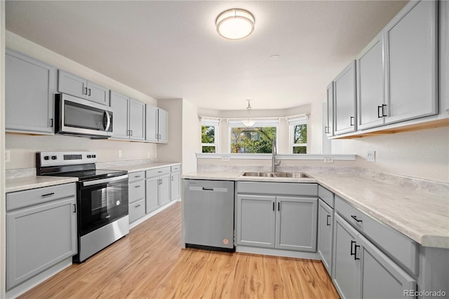 kitchen with sink, gray cabinetry, light hardwood / wood-style flooring, appliances with stainless steel finishes, and pendant lighting