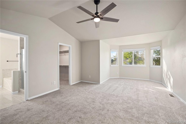 unfurnished bedroom featuring light carpet, ensuite bath, a walk in closet, and ceiling fan