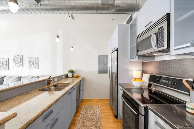 kitchen featuring light stone countertops, appliances with stainless steel finishes, a sink, light wood-style floors, and decorative light fixtures