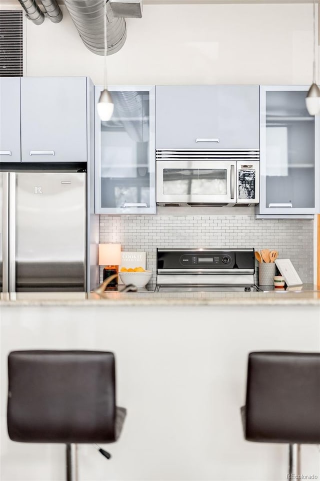 kitchen featuring glass insert cabinets, backsplash, decorative light fixtures, and stainless steel appliances