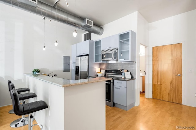 kitchen with a peninsula, light wood-style floors, a kitchen bar, backsplash, and stainless steel appliances