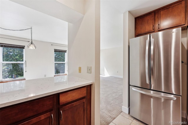 kitchen featuring light stone countertops, pendant lighting, light colored carpet, and stainless steel refrigerator