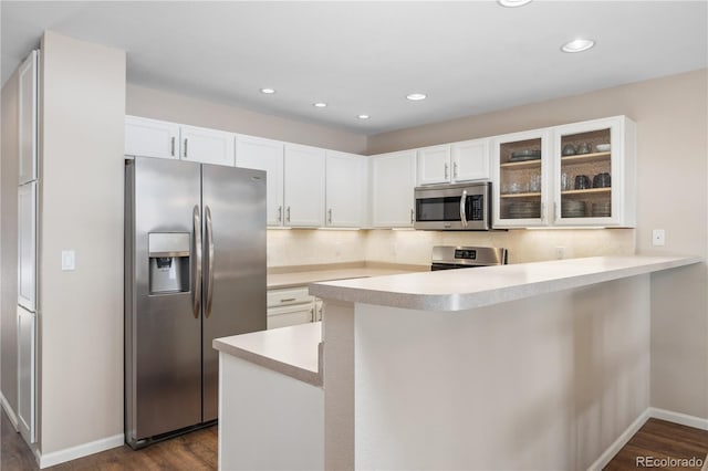 kitchen featuring dark wood finished floors, appliances with stainless steel finishes, glass insert cabinets, a peninsula, and light countertops