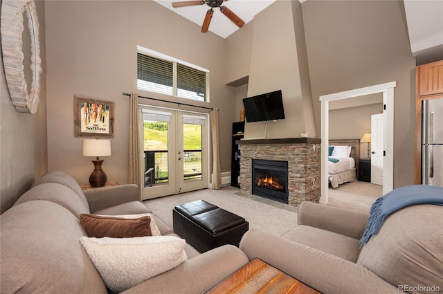 carpeted living room with a stone fireplace, a towering ceiling, and ceiling fan