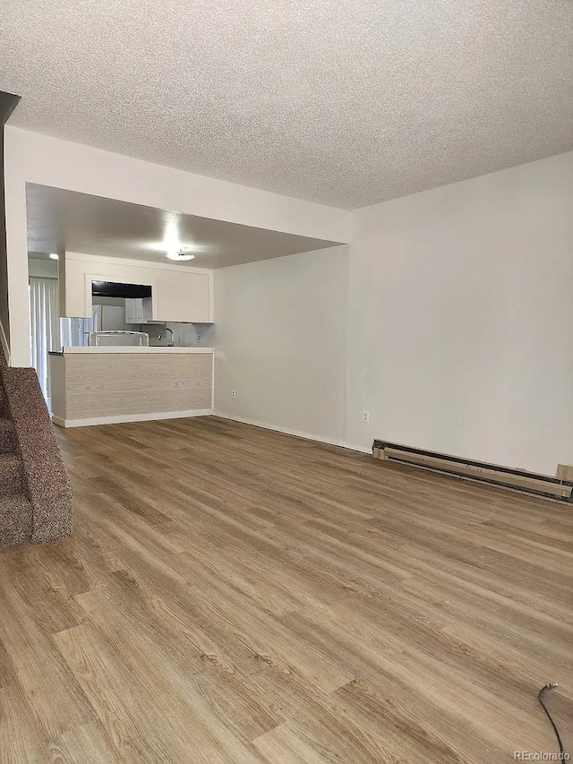 unfurnished living room with baseboard heating, a textured ceiling, and light wood-type flooring