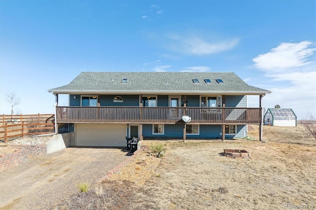 rear view of house with roof with shingles, fence, a garage, driveway, and a fire pit