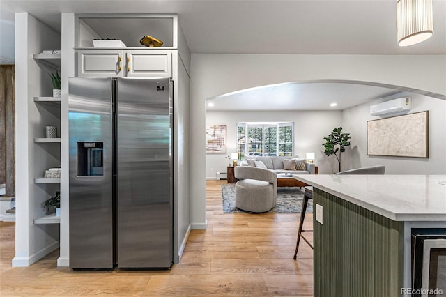 kitchen with light stone countertops, white cabinetry, stainless steel fridge with ice dispenser, a wall unit AC, and light hardwood / wood-style flooring