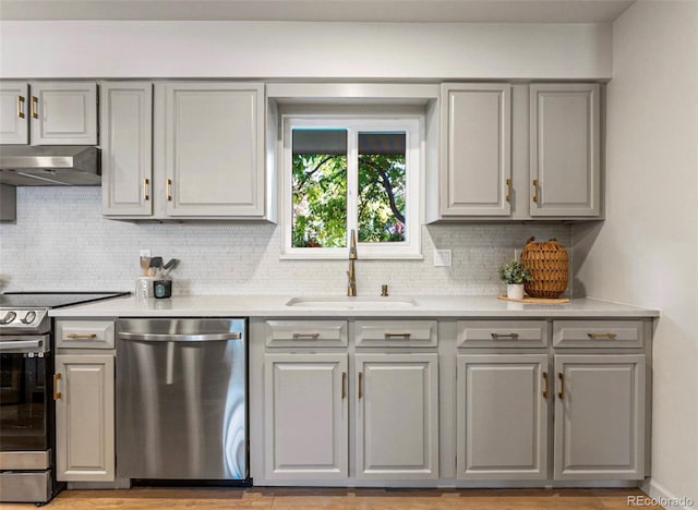 kitchen featuring gray cabinetry, range hood, sink, appliances with stainless steel finishes, and tasteful backsplash