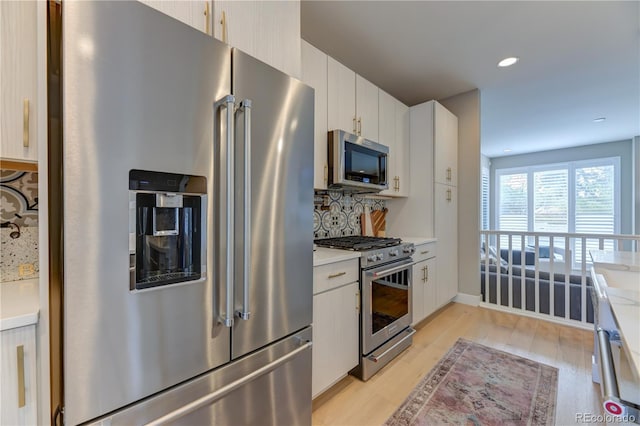 kitchen with high quality appliances, backsplash, white cabinetry, and light hardwood / wood-style flooring