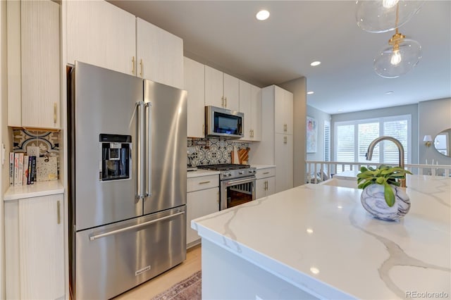 kitchen with premium appliances, light wood-type flooring, pendant lighting, backsplash, and light stone counters