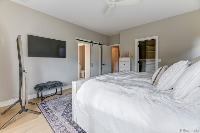 bedroom featuring a walk in closet, a closet, light wood-type flooring, ceiling fan, and a barn door