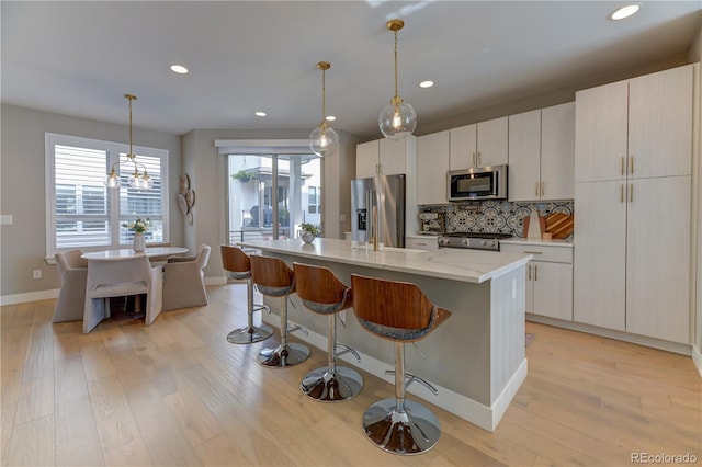 kitchen with light hardwood / wood-style flooring, appliances with stainless steel finishes, decorative light fixtures, tasteful backsplash, and a center island with sink