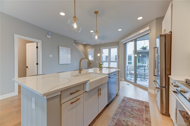 kitchen with high end appliances, white cabinetry, a kitchen island with sink, and decorative light fixtures