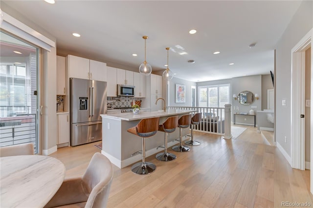 kitchen with appliances with stainless steel finishes, white cabinetry, tasteful backsplash, hanging light fixtures, and a kitchen island with sink