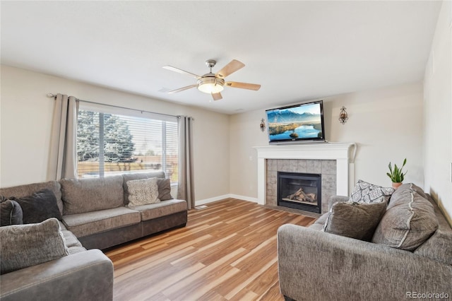 living room featuring a tile fireplace, light hardwood / wood-style flooring, and ceiling fan