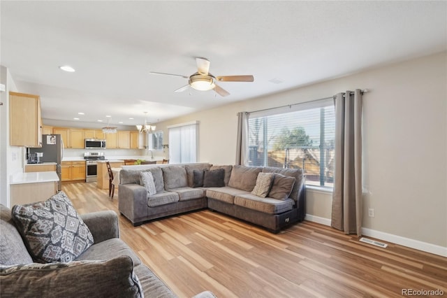 living room with light hardwood / wood-style floors and ceiling fan with notable chandelier