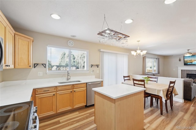 kitchen with stainless steel dishwasher, hanging light fixtures, sink, a tiled fireplace, and stove