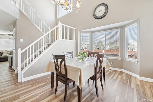 dining area with ceiling fan with notable chandelier, a healthy amount of sunlight, light hardwood / wood-style flooring, and a towering ceiling