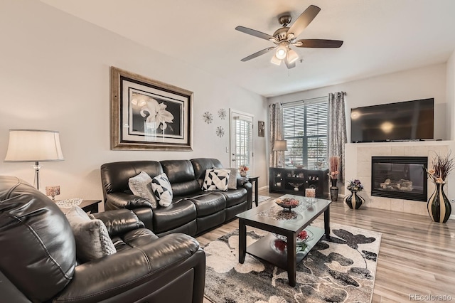 living room featuring a tile fireplace, baseboards, ceiling fan, and wood finished floors