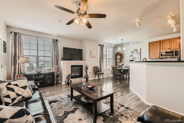 living area featuring visible vents, light wood-style flooring, a tile fireplace, and a textured ceiling