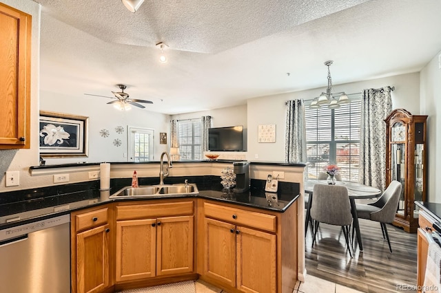 kitchen with a peninsula, stainless steel dishwasher, brown cabinetry, a textured ceiling, and a sink