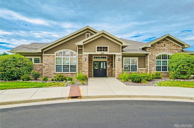 craftsman-style house featuring stone siding and a shingled roof