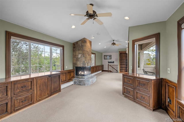 carpeted living room with a healthy amount of sunlight, vaulted ceiling, a stone fireplace, and a baseboard heating unit