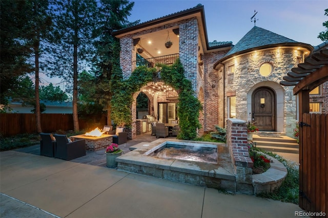 back house at dusk featuring an in ground hot tub, an outdoor living space with a fire pit, and a patio