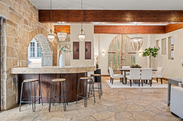 kitchen featuring beam ceiling, a kitchen breakfast bar, a chandelier, and pendant lighting