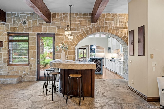 kitchen featuring a breakfast bar area, appliances with stainless steel finishes, beam ceiling, and decorative light fixtures