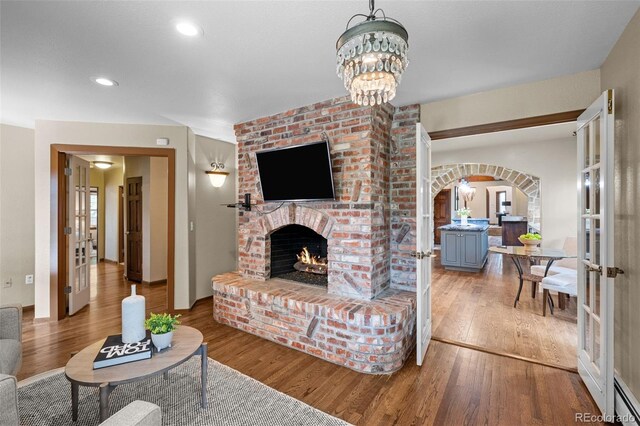 living area featuring arched walkways, a brick fireplace, french doors, and wood finished floors