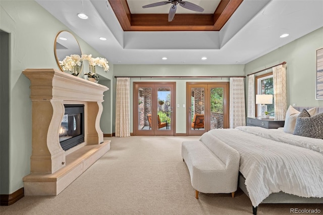 carpeted bedroom with recessed lighting, access to outside, a tray ceiling, and a glass covered fireplace