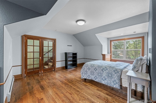 bedroom featuring a baseboard heating unit, baseboards, wood finished floors, and lofted ceiling