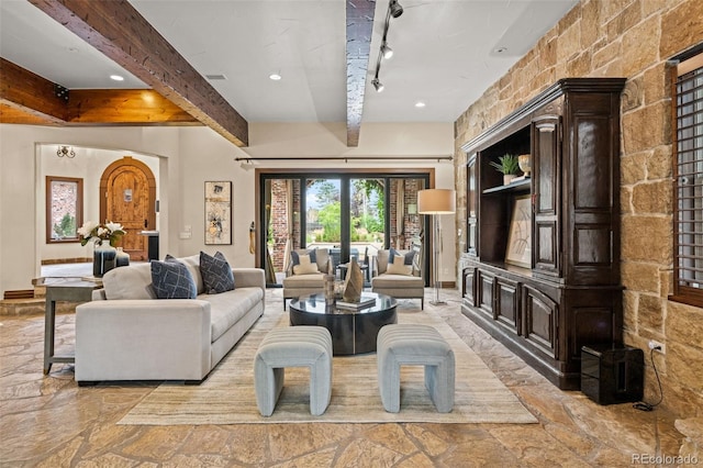 living area featuring stone finish flooring, beamed ceiling, rail lighting, and visible vents