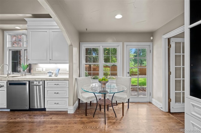 bar featuring baseboards, a sink, stainless steel dishwasher, and wood finished floors