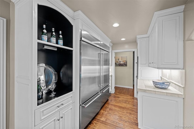 kitchen with recessed lighting, light wood-style floors, white cabinets, tile counters, and stainless steel built in fridge