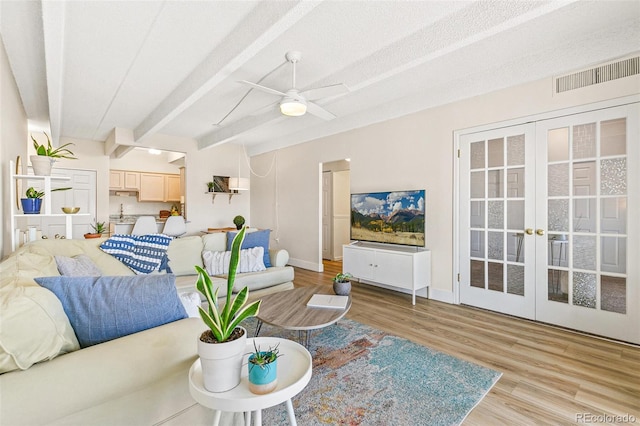 living room featuring french doors, light wood-type flooring, a textured ceiling, ceiling fan, and beamed ceiling